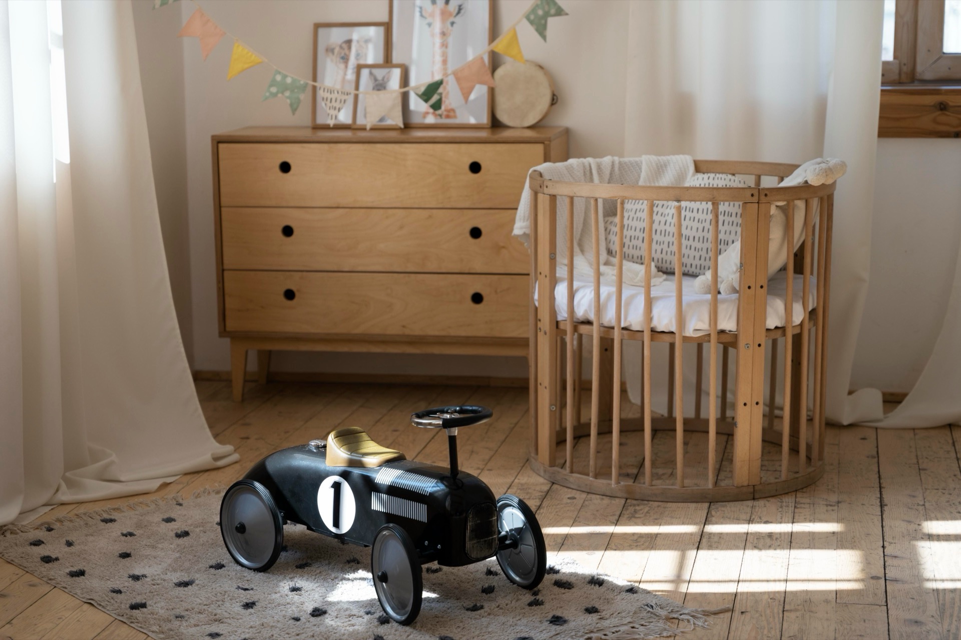 Ljust babyrum med spjälsäng i trä, byrå och en leksaksbil på mattan