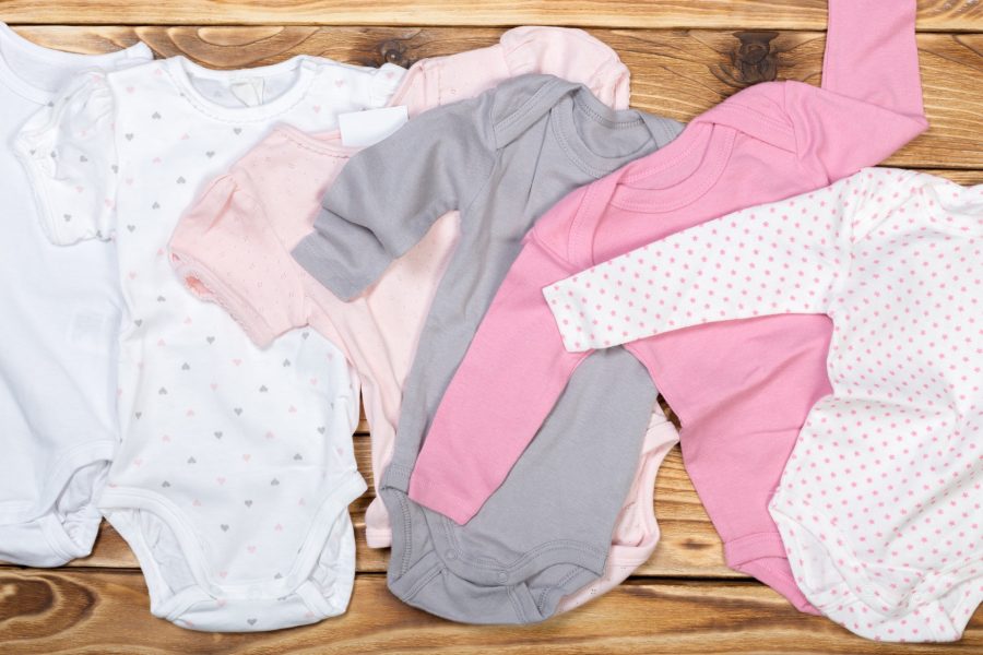 Babybodys och pyjamasar i rosa, grått och vitt utbredda på ett träbord